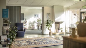 A spacious lobby with a blue armchair, a patterned rug, and several potted plants.