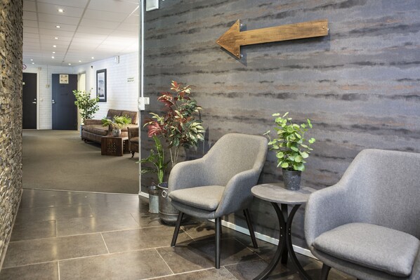 A lobby area with two grey armchairs, a small table, and potted plants. A wooden arrow sign points to the left. - Hotell Solhem Park (Borås)