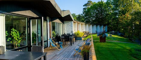 A modern outdoor patio with a wooden deck, glass-enclosed seating area, and a well-maintained lawn.