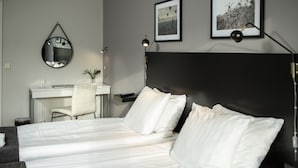 A hotel room with a bed, a desk, a chair, a mirror, and two framed pictures on the wall.