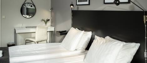 A hotel room with a bed, a desk, a chair, a mirror, and two framed pictures on the wall.