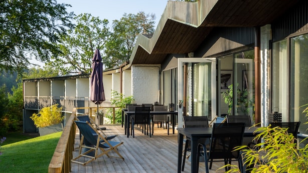 An outdoor patio with wooden flooring, a dining table, chairs, and a cushioned lounge chair.