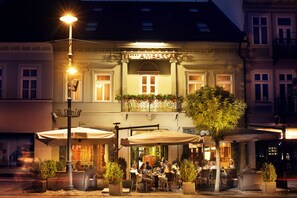 Un hotel con terraza exterior, un balcón con flores y una fachada bien iluminada.