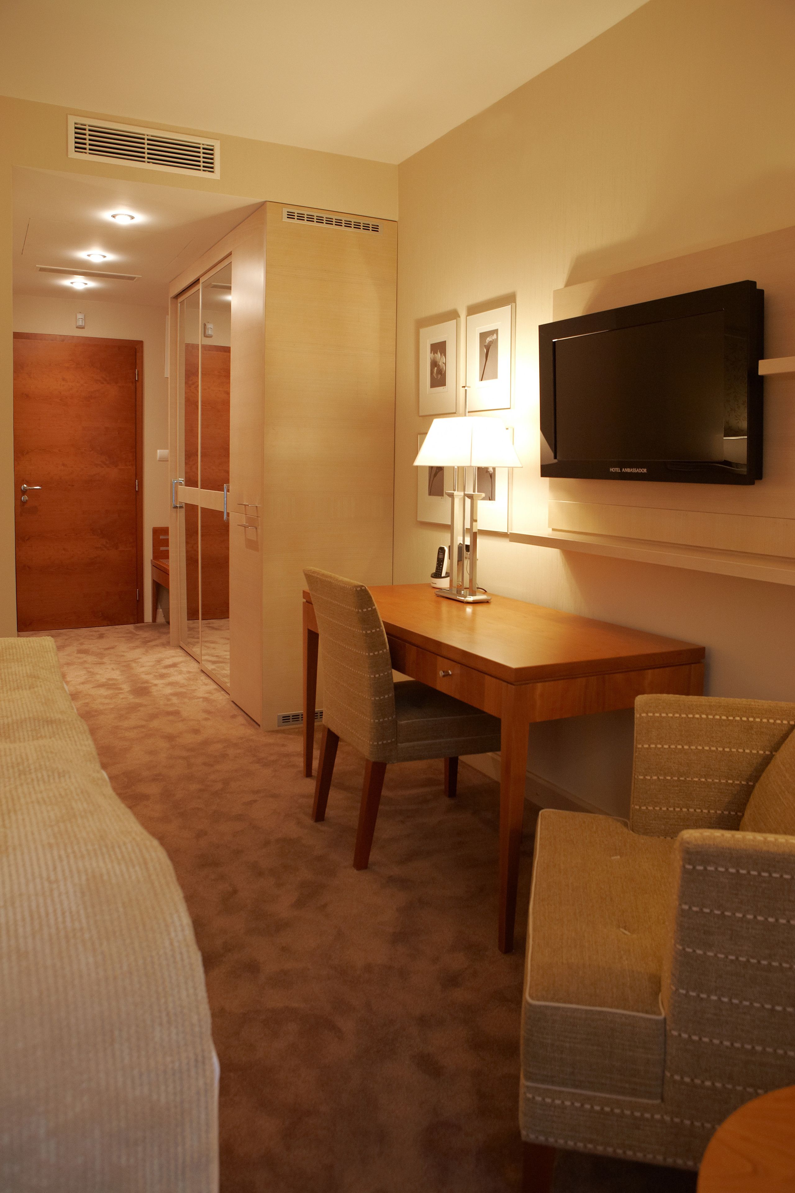 A hotel room with a bed, a desk with a chair, a television, and a door leading to another room.