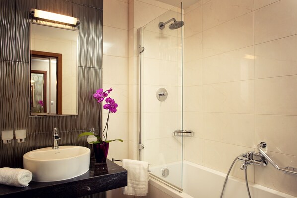 Un baño moderno con ducha de vidrio, lavamanos blanco y un espejo encima.