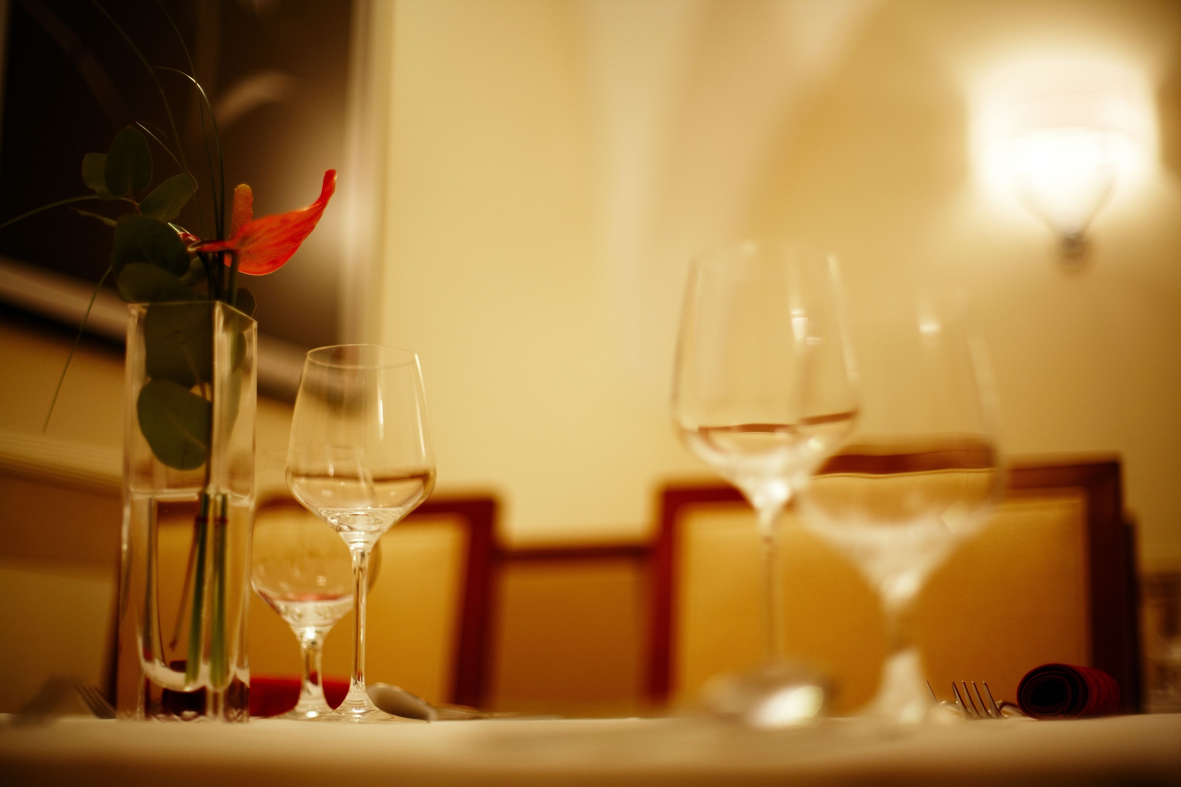 Una mesa de comedor con tres copas de vino y un jarrón con una flor roja.