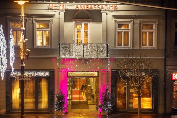 A hotel facade with a balcony, illuminated entrance, and Christmas decorations.
