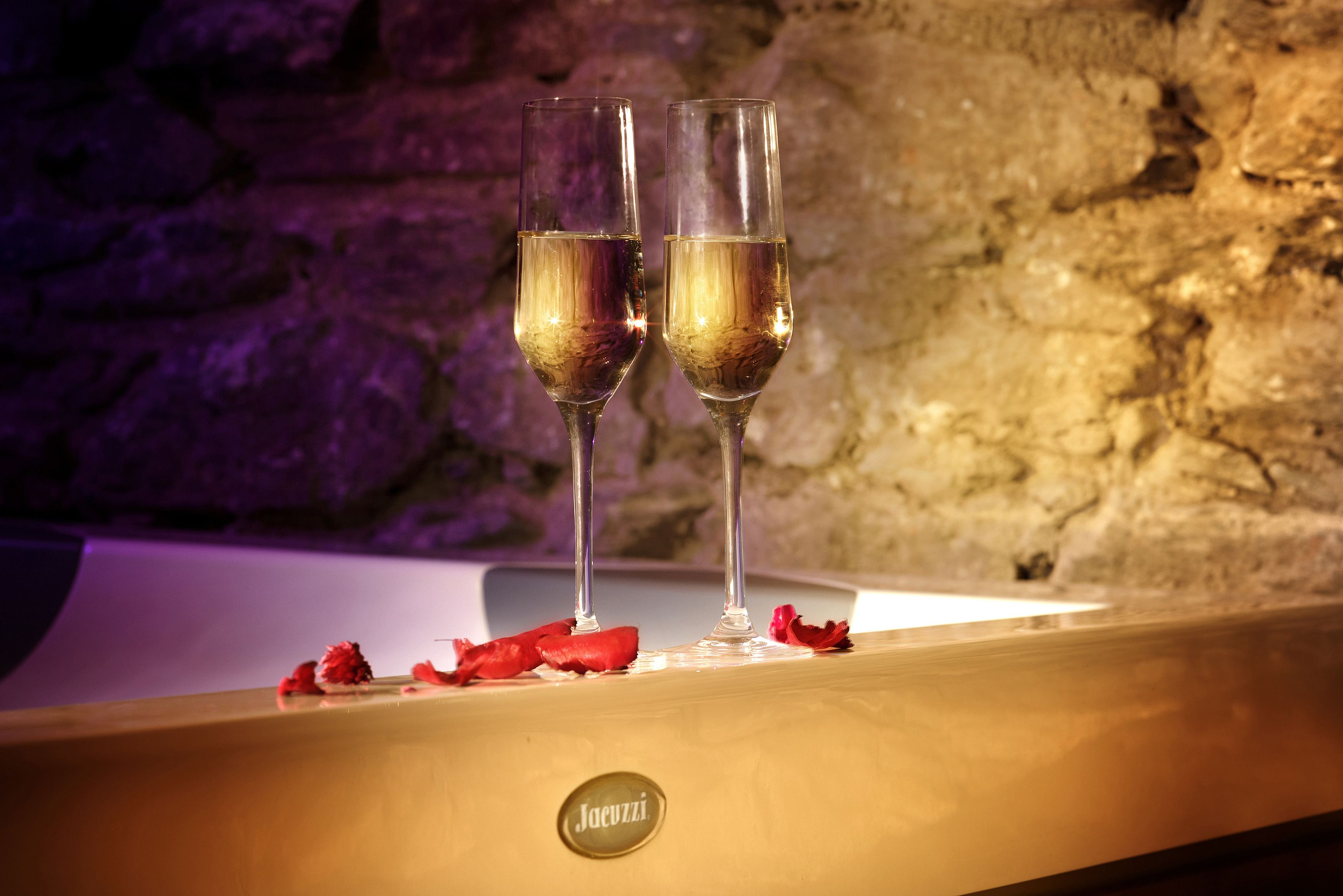 Two glasses of champagne on a bar counter with a stone wall background.