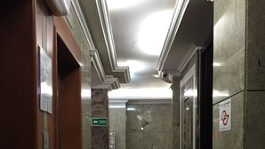 Un pasillo con piso de mármol, una columna de mármol, un bote de basura y una puerta con un letrero.