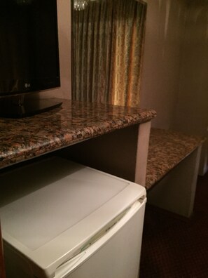 Una cocina con encimera de granito, un refrigerador blanco y una ventana con cortinas estampadas.