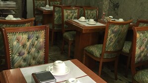 Un comedor con mesas y sillas de madera, equipado con tazas y platillos blancos, y un reloj en la pared.