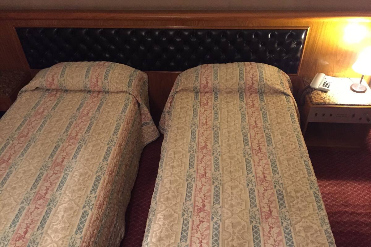Two beds with patterned bedding, a headboard, a bedside table with a lamp, and a telephone.