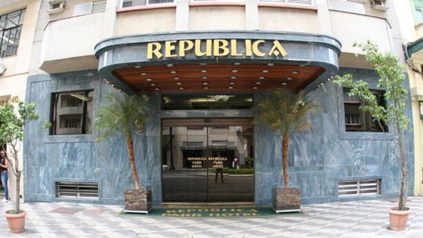 Exterior del Hotel Republica Park, con una entrada curva, dos palmeras y un pavimento adoquinado.