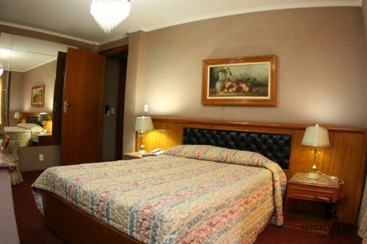 A hotel room with a large bed, two bedside tables with lamps, a painting on the wall, and a door leading to another room.