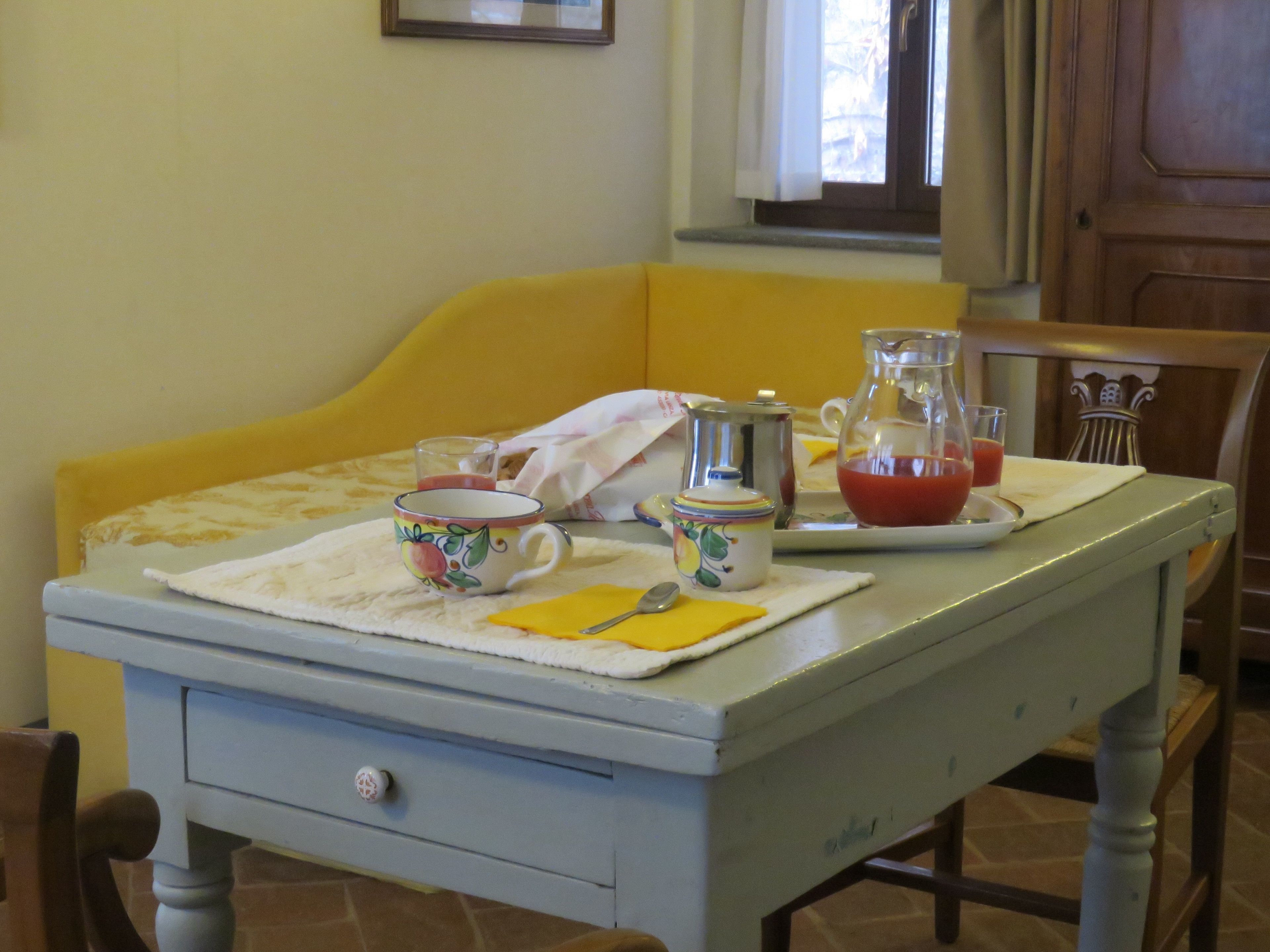 A dining table with a pitcher, a cup, and a plate with a glass of red liquid, set on a tablecloth.