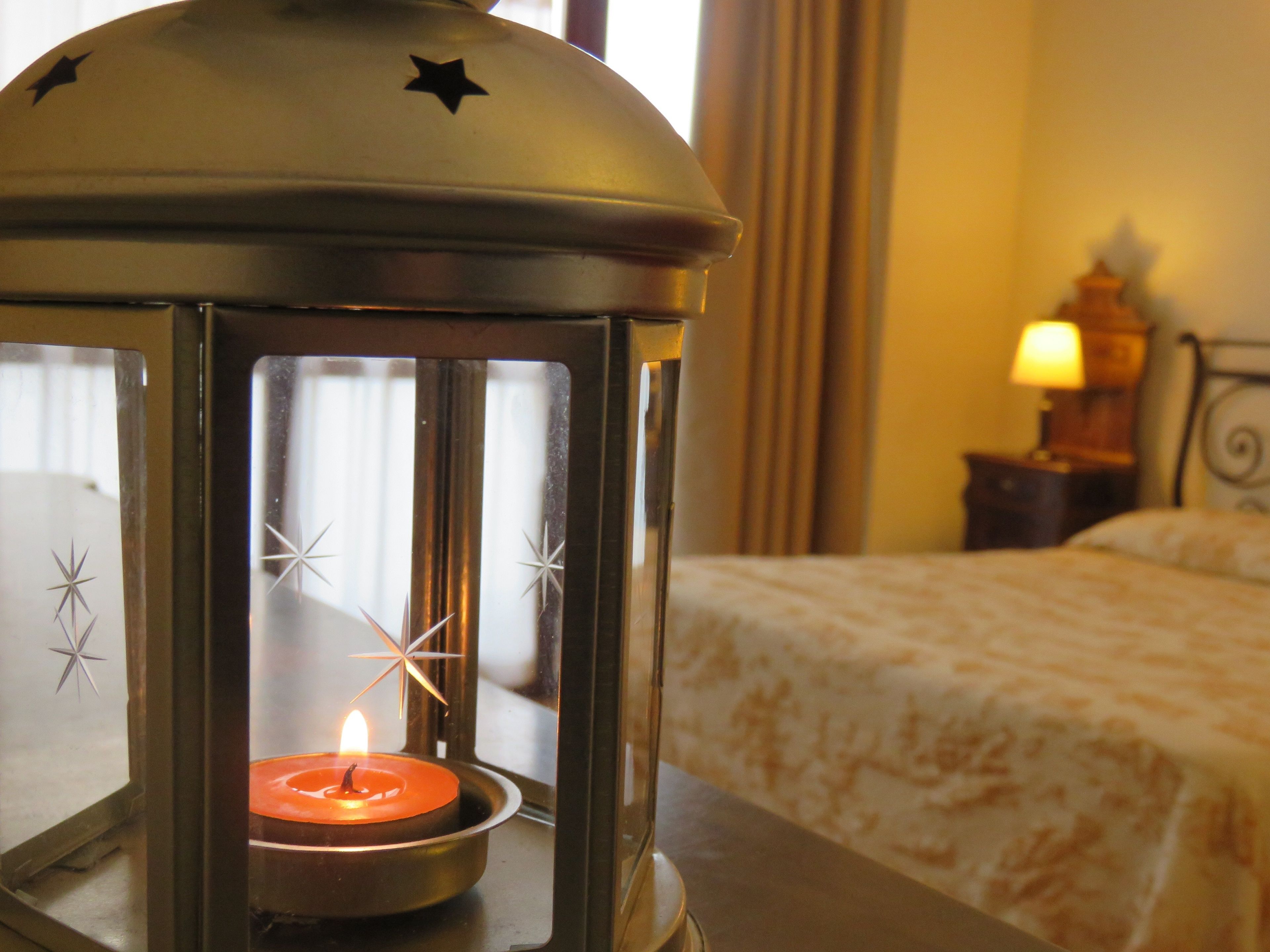 A lantern with a lit candle inside, placed on a table in a hotel room.