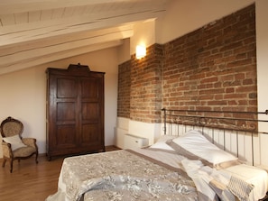 Une chambre à coucher avec un lit, une armoire en bois, une chaise et un mur en briques.