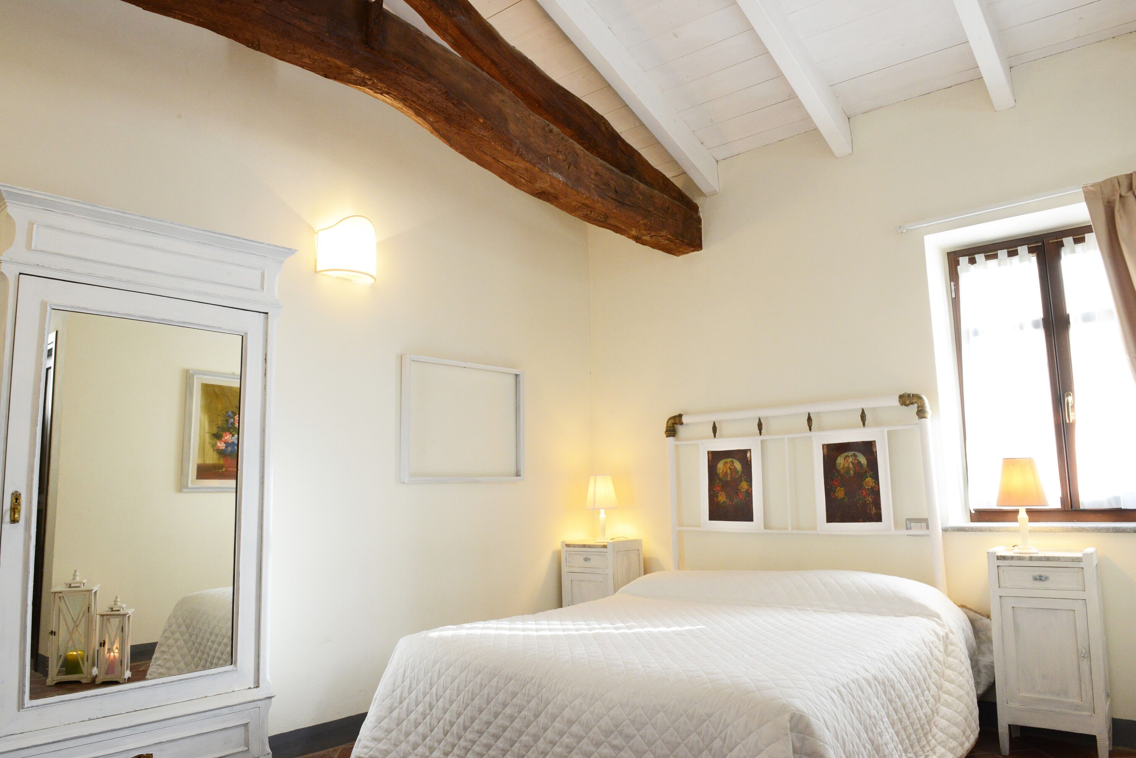 Een slaapkamer met een groot bed, een kledingkast, een spiegel en een raam met gordijnen.