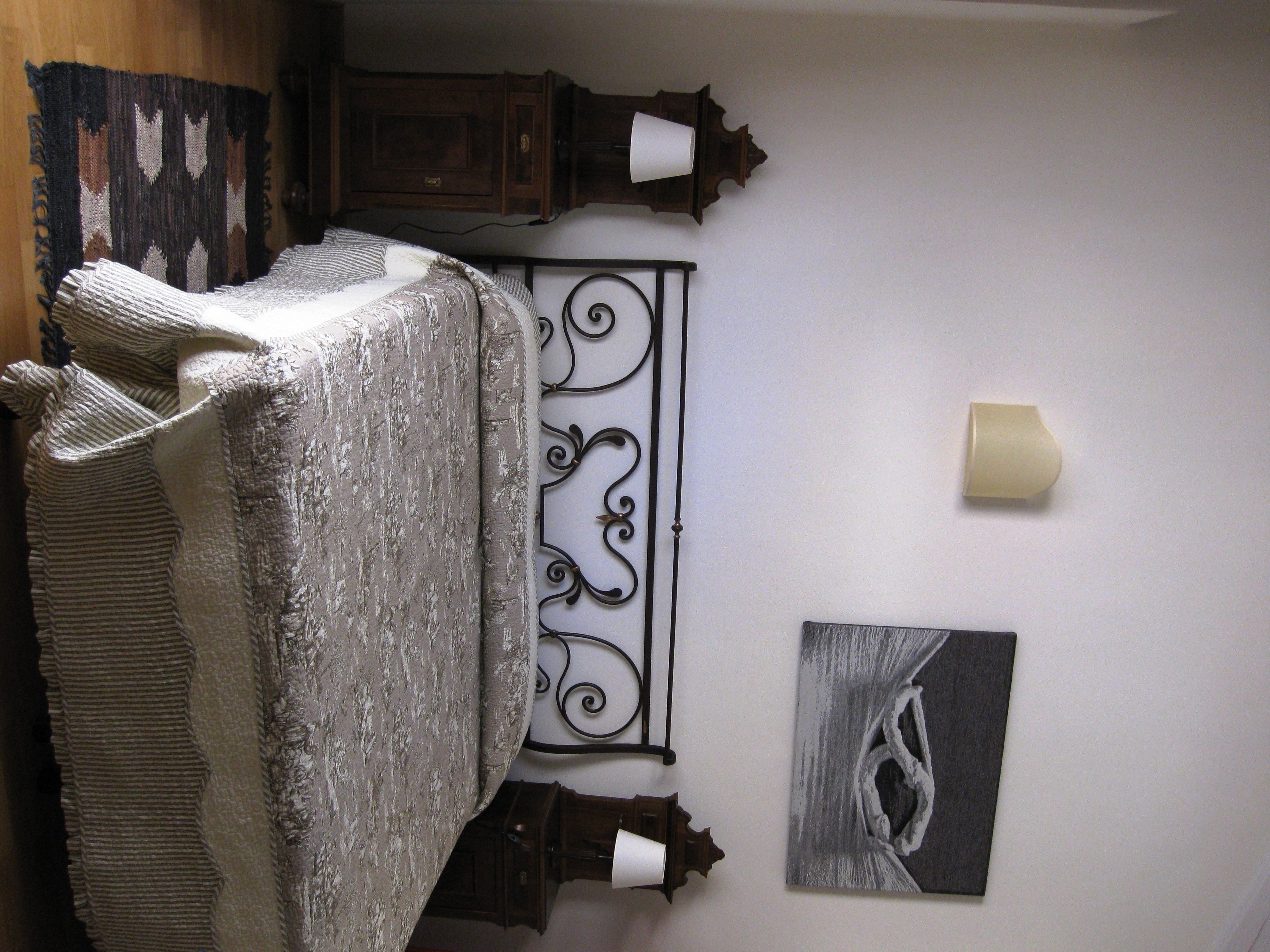 Ein Zimmer mit einem Bett, das mit einer gemusterten Decke bezogen ist, einem dekorativen Wandelement aus Metall und einem gerahmten Kunstwerk.