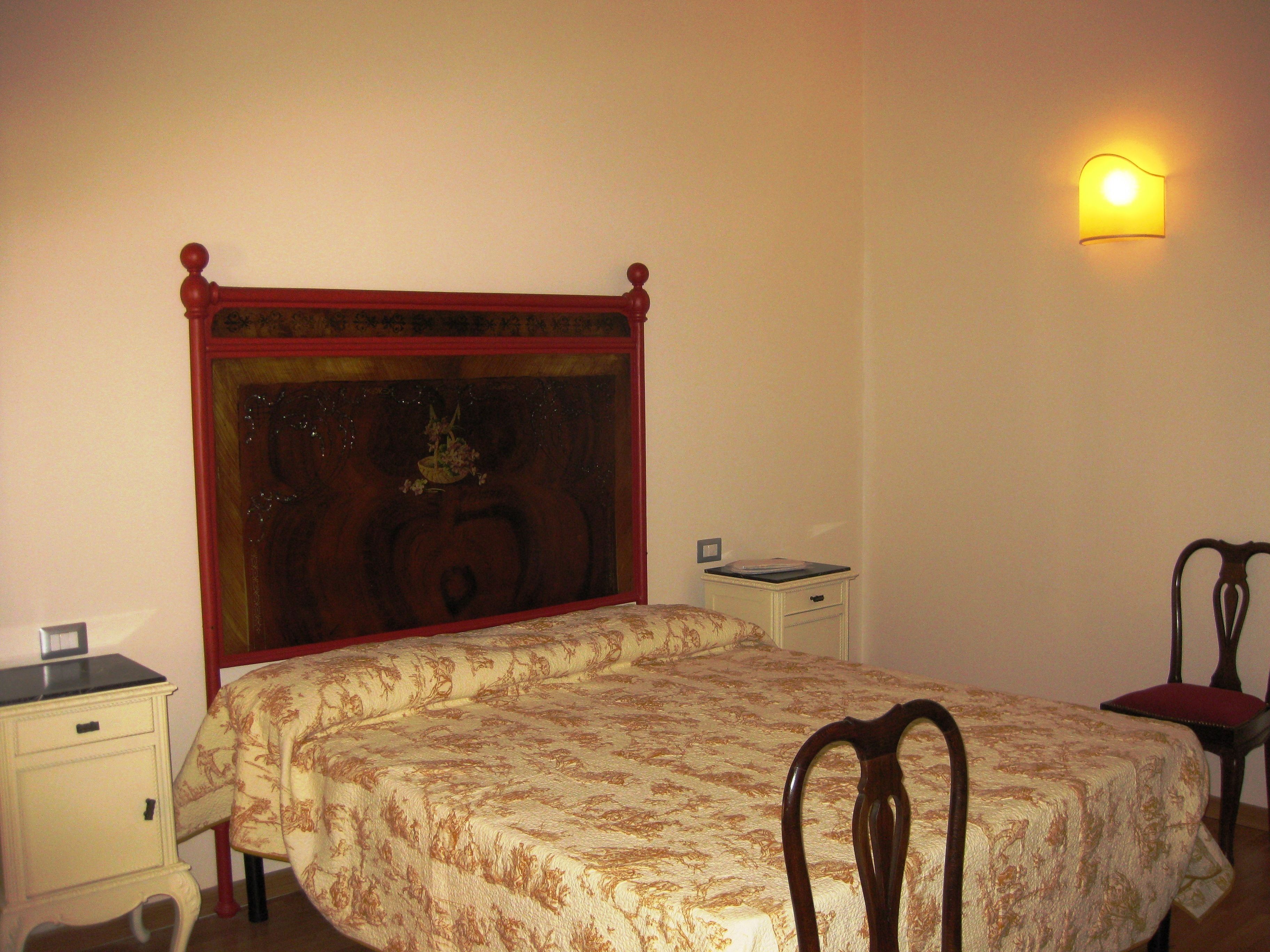 A bedroom with a wooden bed frame, a nightstand, a chair, and a wall-mounted light.