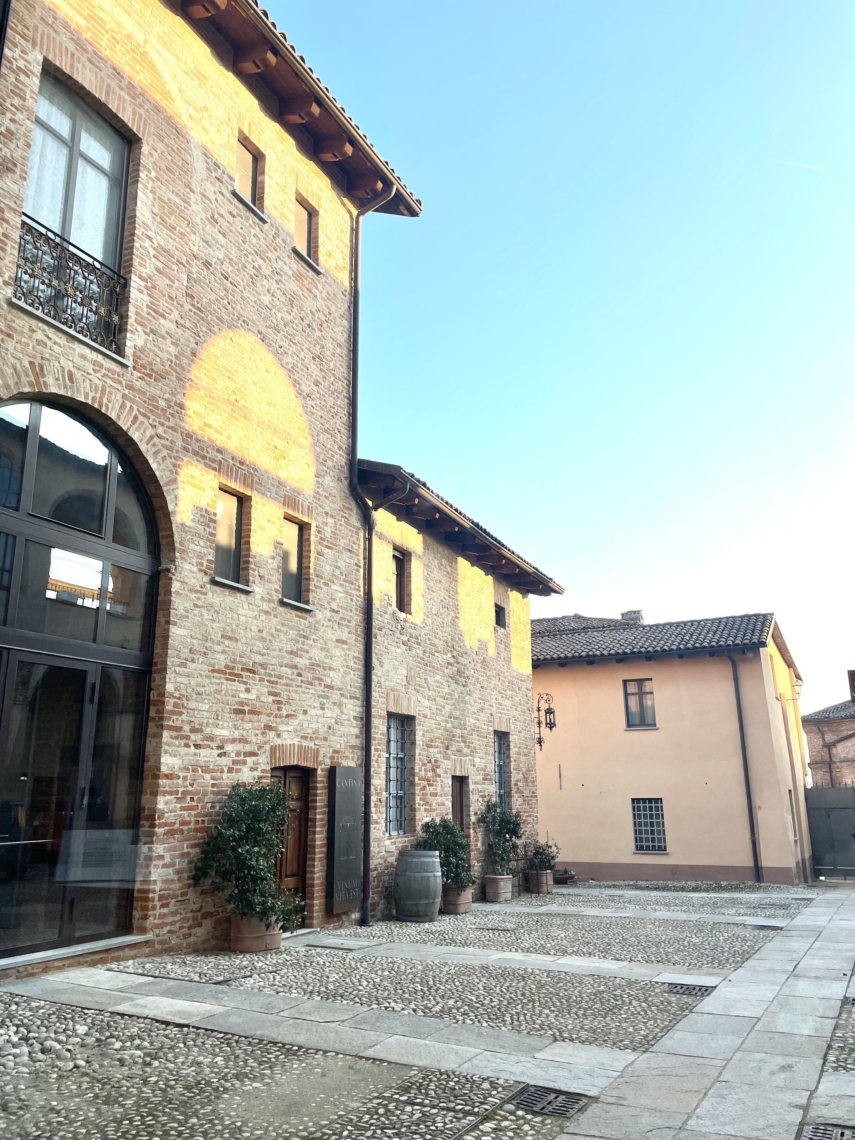 Un patio con un edificio de fachada de ladrillo, amplias ventanas y suelo empedrado de piedra.