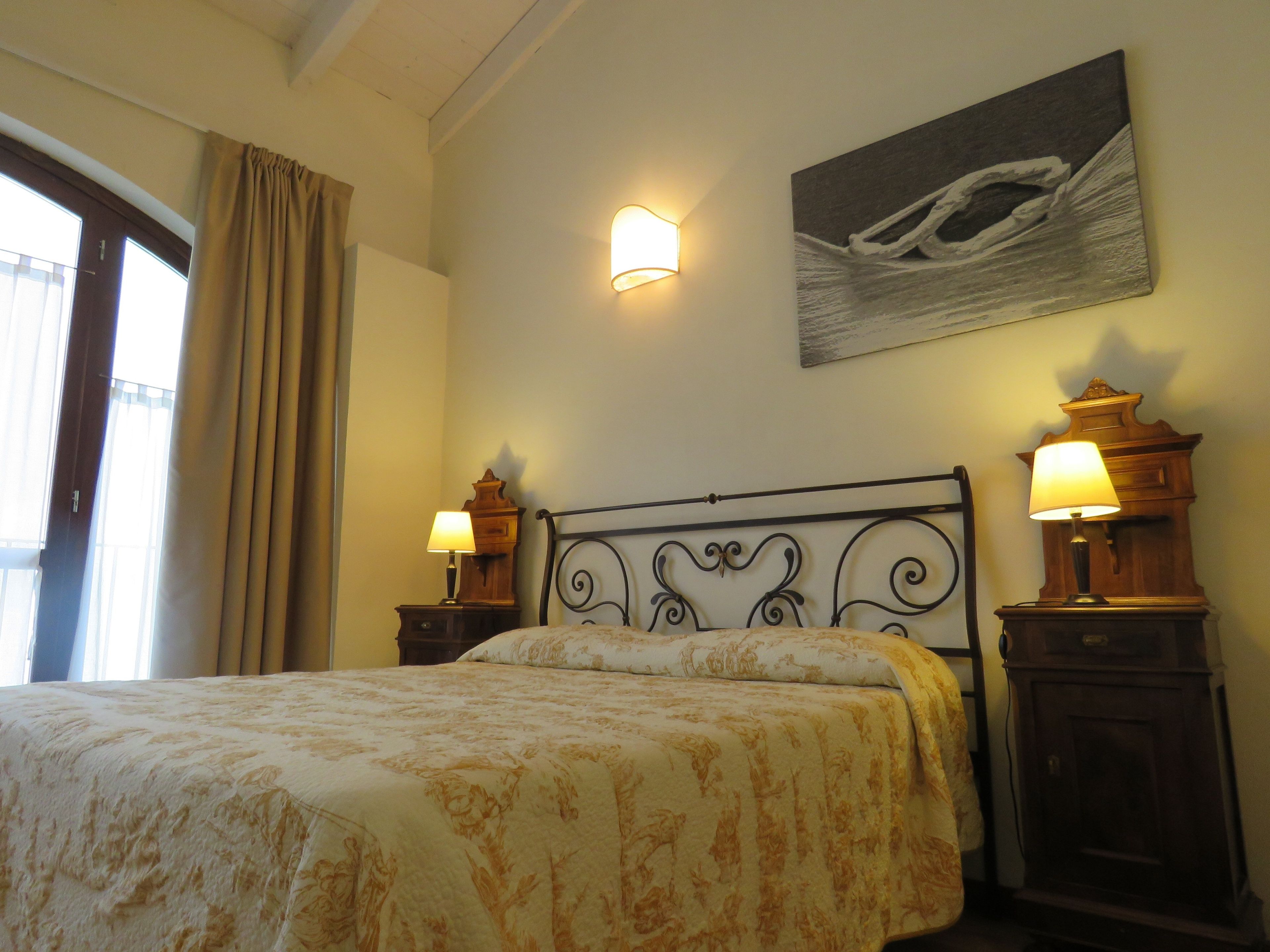 A bedroom with a bed, two bedside lamps, a wall-mounted light, and a painting.