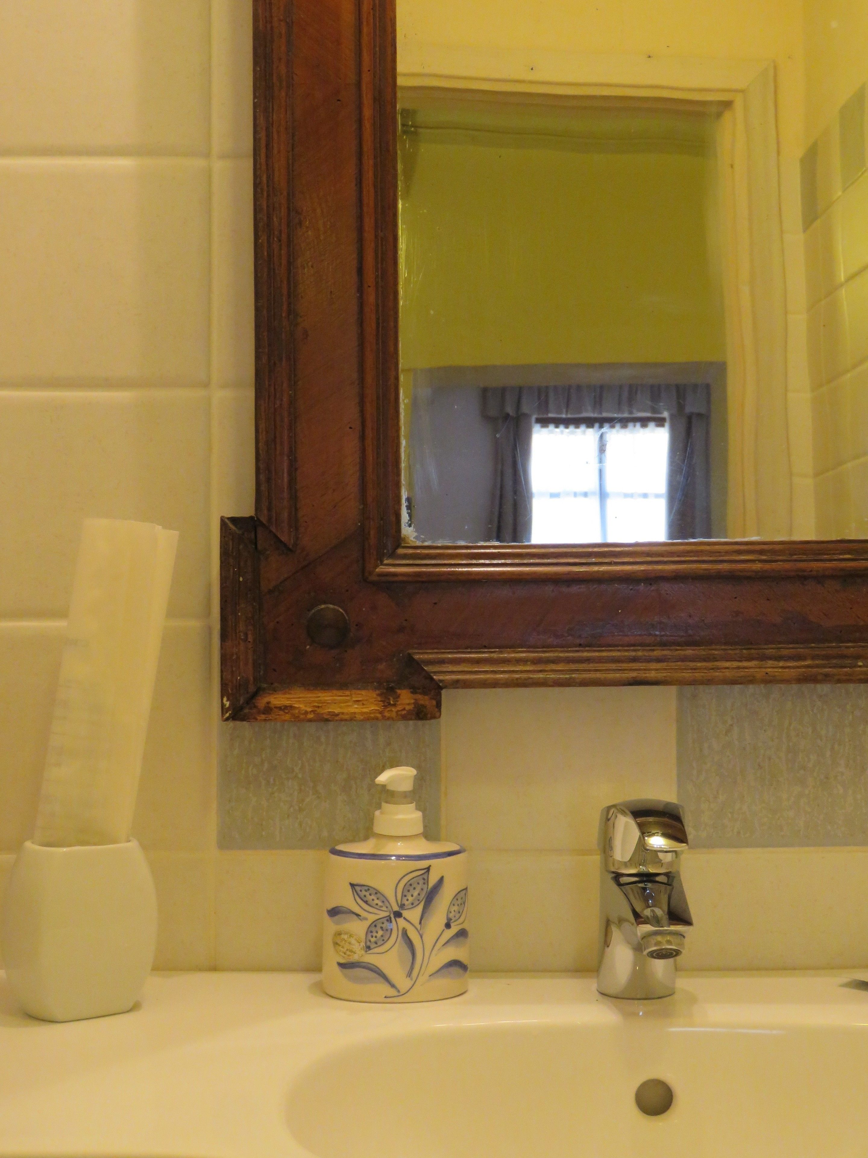 Un baño con un lavamanos blanco, un espejo y una ventana con cortinas.