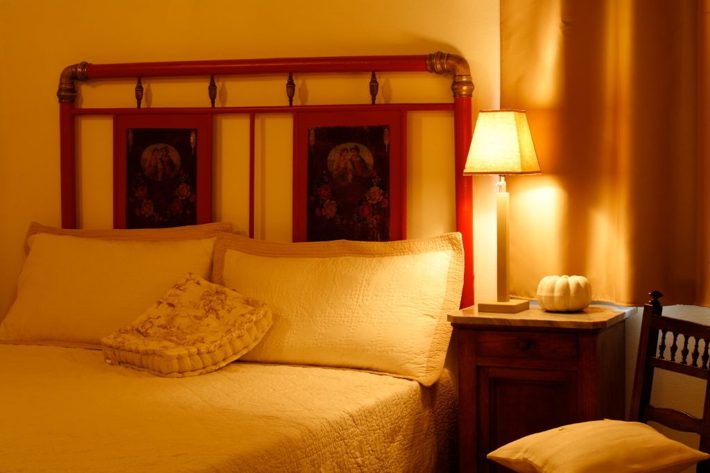 Una cama con cabecera de madera, una mesita de noche con una lámpara y una silla.
