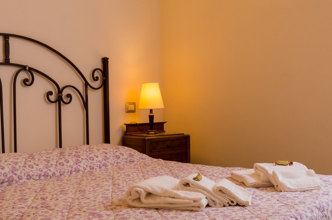 A neatly made bed with a floral-patterned bedspread, a bedside lamp, and folded towels on the nightstand.