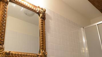 Ein Badezimmer mit einem großen, verzierten Spiegel, weißen Fliesenwänden, einem weißen Waschbecken und einer roten Kerze.