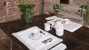 A rustic brick wall with a wooden table set for dining, featuring a lantern, plates, cups, and cutlery. - Relais Palazzo Paleologi - Secolo XIV (Lu e Cuccaro Monferrato)