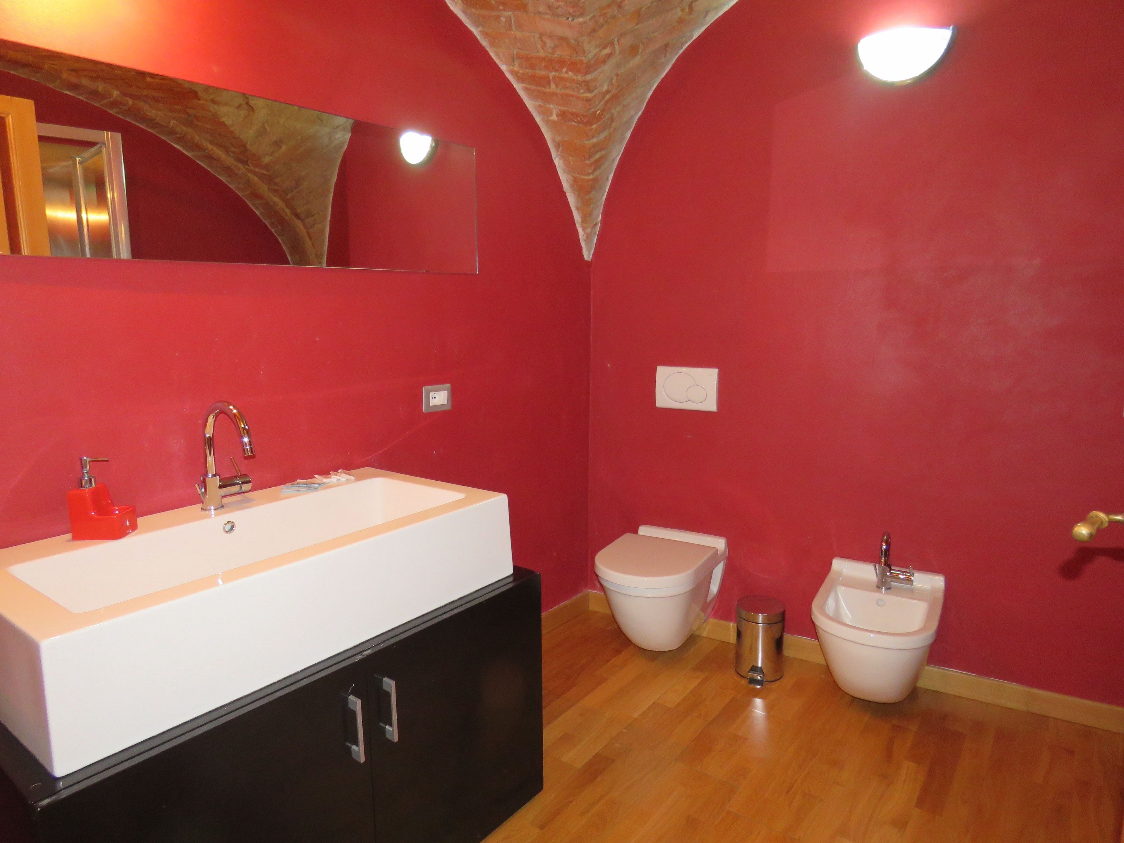 Een badkamer met een witte wastafel, een toilet en een bidet. Boven de wastafel hangt een spiegel en aan het plafond een lamp.