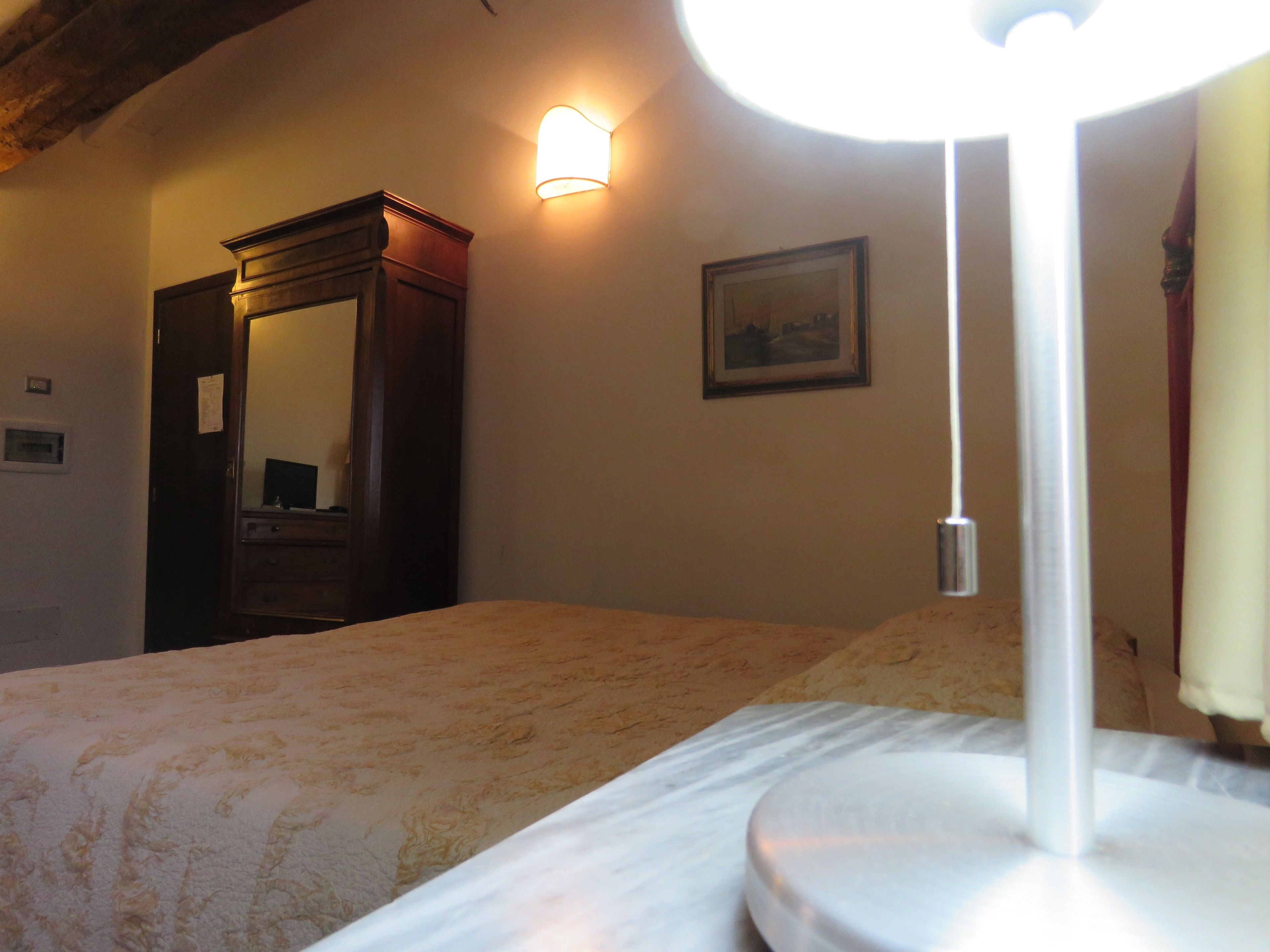 Une chambre à coucher comprenant un lit, une table de chevet, un miroir, une lampe fixée au mur et un tableau encadré.