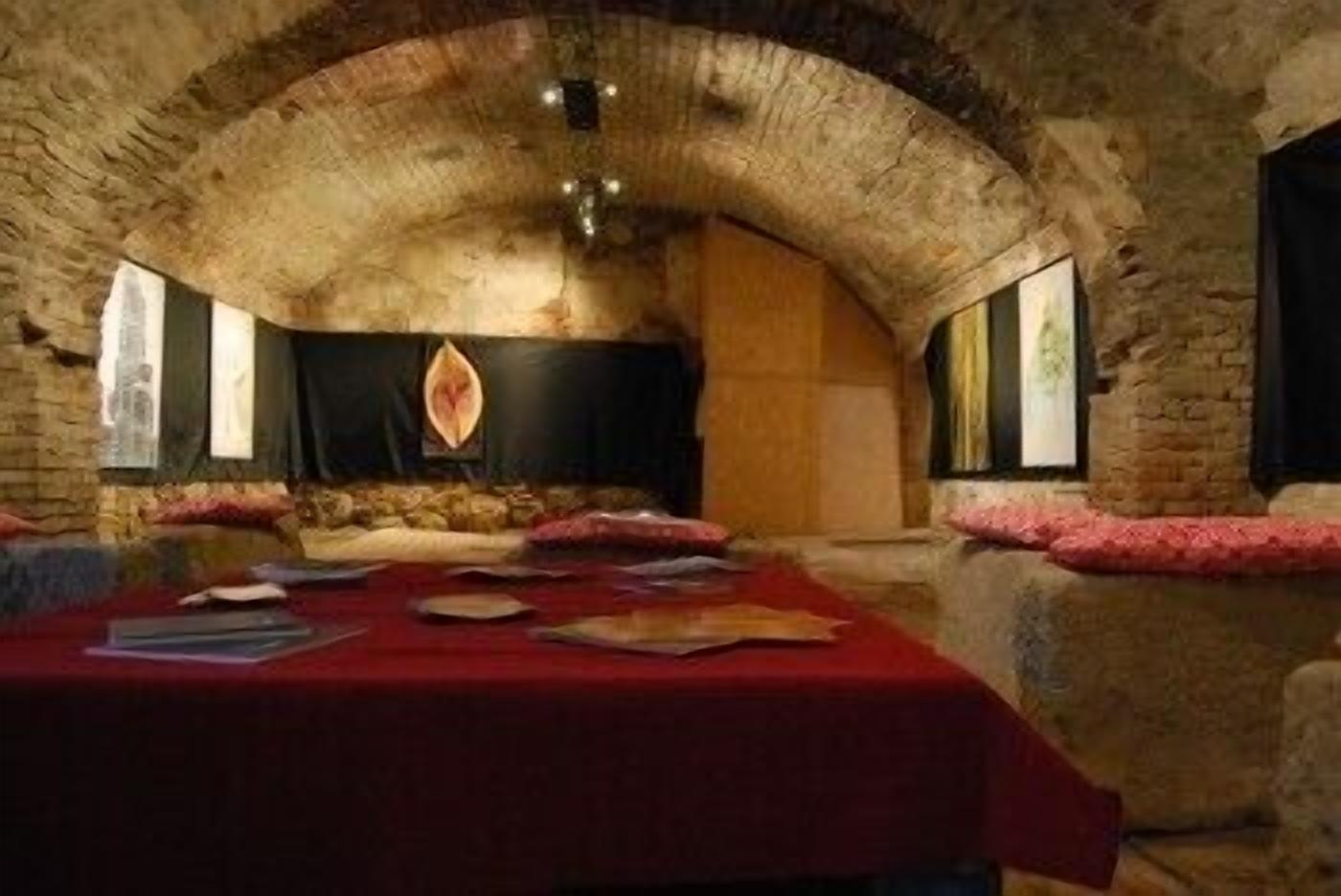 A room with a stone vaulted ceiling, a long table with a red tablecloth, and a stone fireplace.