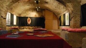 A room with a stone vaulted ceiling, a long table with a red tablecloth, and a stone fireplace.