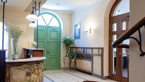 Un vestíbulo de hotel con una mesa de recepción, una puerta verde, una escalera y un comedor.