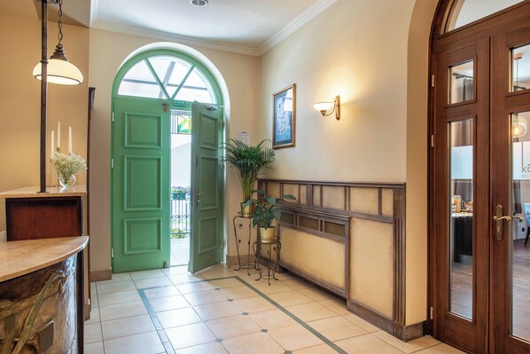 Un pasillo con una puerta verde, una recepción, una planta en maceta y un cuadro en la pared.