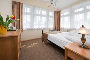 A hotel room with a bed, a bedside table with a lamp, a wooden desk with a vase of flowers, and a radiator. - Villa Sedan - Destigo Hotels (Sopot)