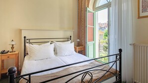 Un dormitorio con una cama, una mesita de noche con lámpara, una ventana con cortinas y vistas a edificios.