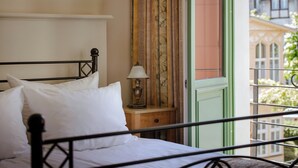 Una cama con ropa de cama blanca, una lámpara de noche y una ventana con cortinas.