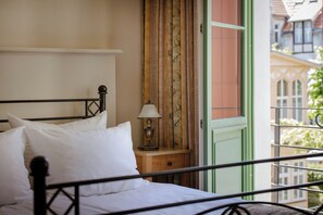 A bed with white bedding, a bedside table with a lamp, and a view of buildings through a window. - Villa Sedan - Destigo Hotels (Sopot)