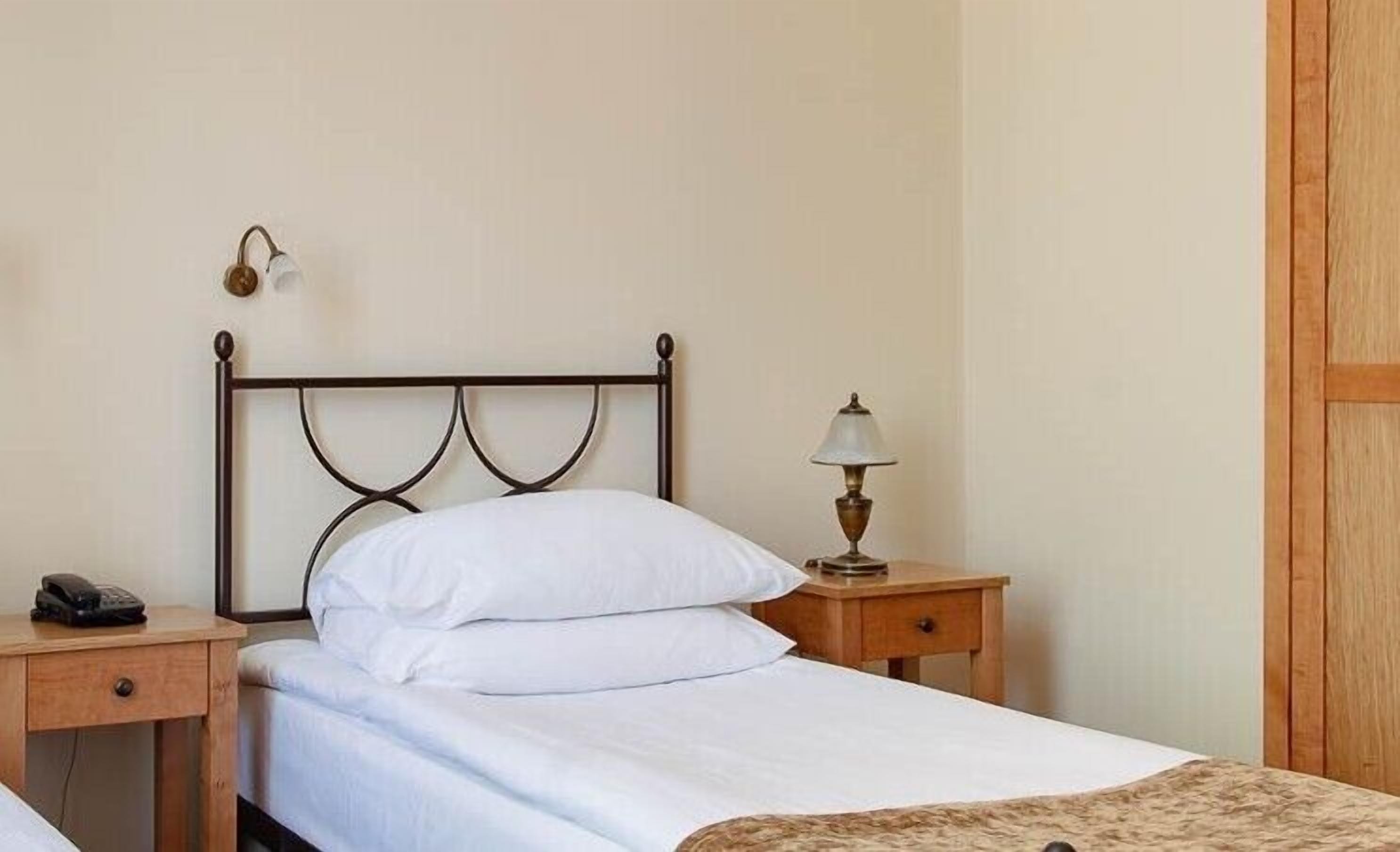 A neatly made bed with white linens, a bedside lamp, and a phone on a wooden nightstand.