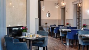 Interior de restaurante con sillas tapizadas en azul, mesas con cubierta de mármol, lámparas colgantes y chimenea.