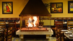 A restaurant with a brick fireplace, wooden tables, and chairs. - Le Cedrus Hotel (Al Arz)