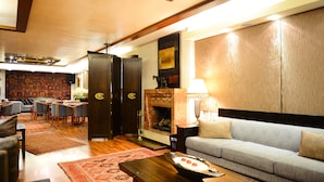 A modern living room with a sofa, coffee table, and a fireplace. There is a dining area with chairs and a table. - Le Cedrus Hotel (Al Arz)