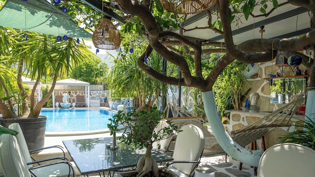 Un área junto a la piscina con una mesa de vidrio, sillas y una hamaca.