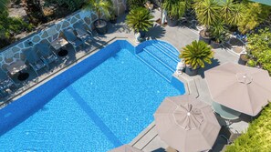 Una piscina con borde de piedra, rodeada de sillas de descanso y sombrillas.