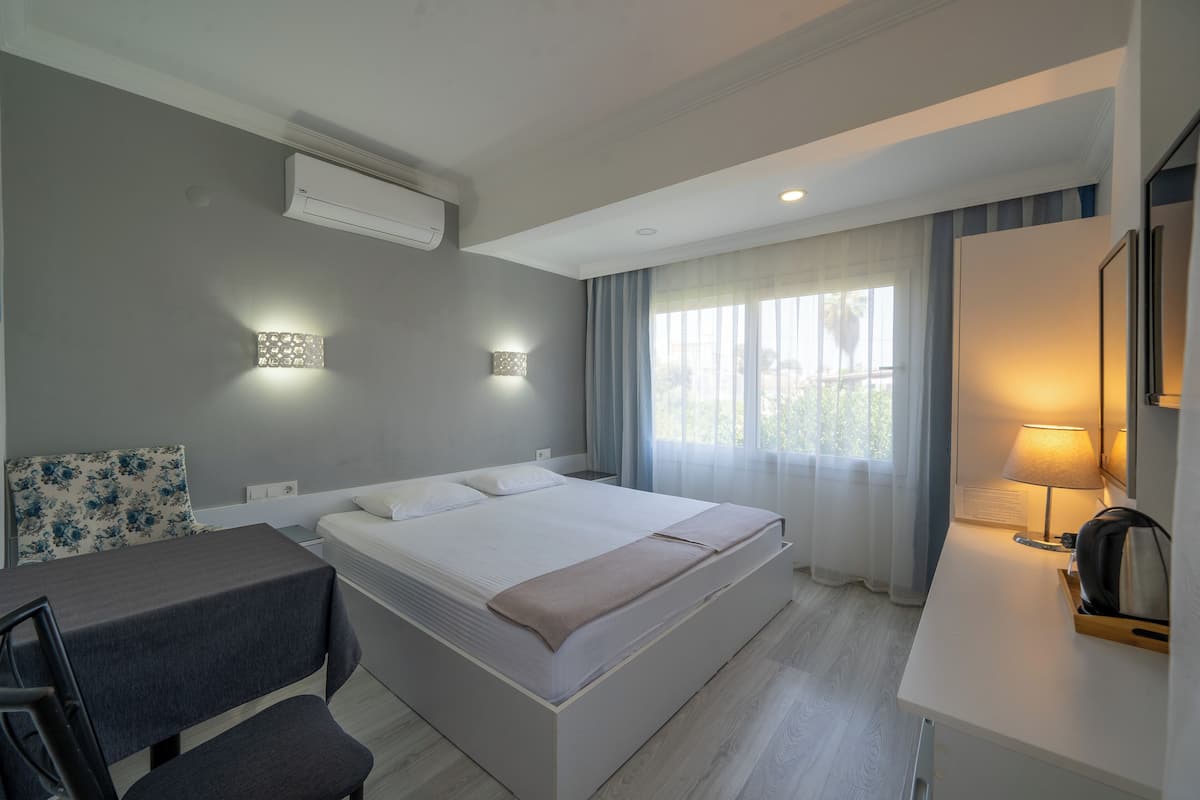 Una habitación de hotel moderna con cama, mesita de noche, lámpara y vistas al exterior.