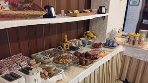 Ein reichhaltiges Buffet mit verschiedenen Speisen, darunter Gebäck, Früchte und Beilagen, auf einem Tisch mit gefliestem Boden und Holzvertäfelung im Hintergrund.