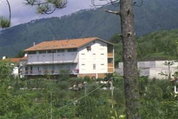 A two-story building with a flat roof, surrounded by greenery and mountains in the background. - Albergo Ristorante La Greppia (Podenzana)